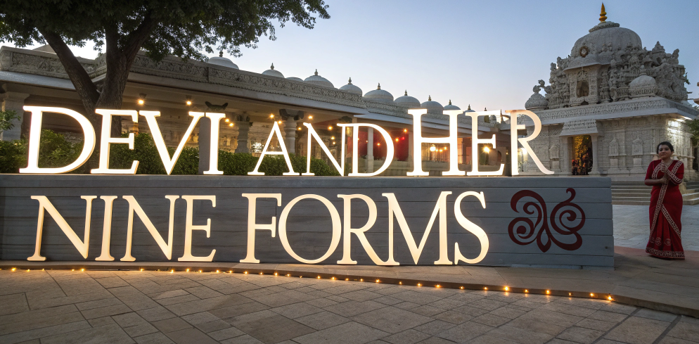 Illuminated sign reading ‘Devi and Her Nine Forms’ outside a temple, symbolizing nau deviyon ke naam and navratri 9 devi names from Shailaputri to Siddhidatri in Navdurga tradition